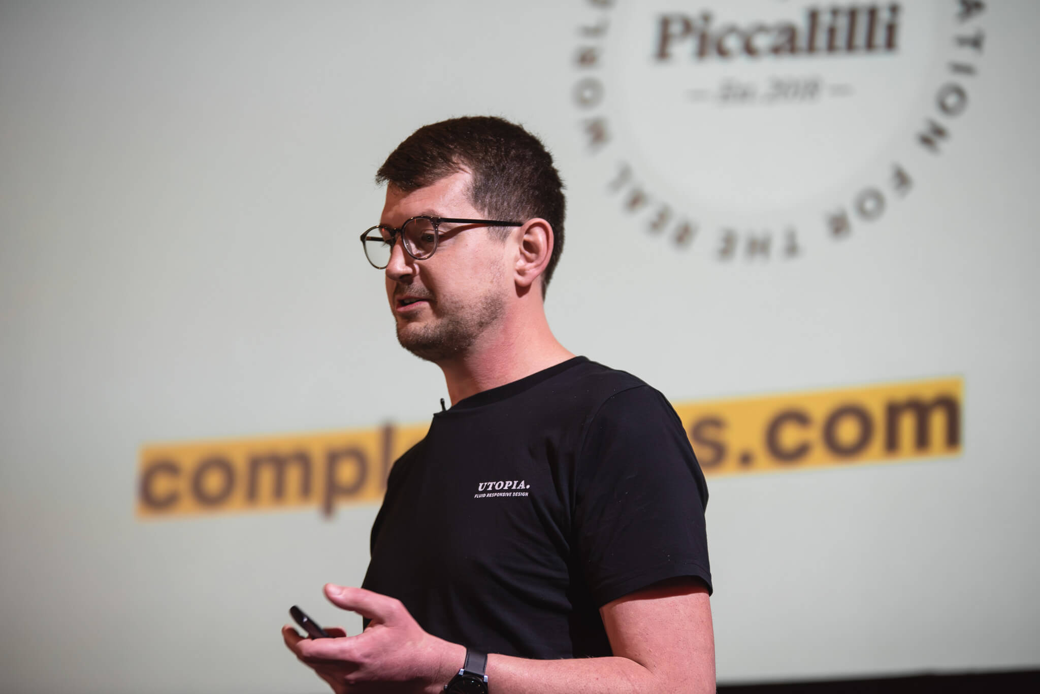 Andy Bell presenting from the stage with a slide behind him with the Piccalilli logo